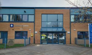 Image shows photo of the outside of the Oxford Centre building, showing the front entrance and signage.